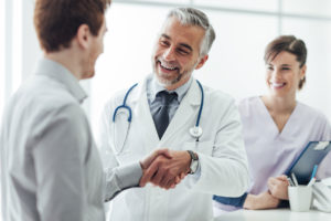 A photo of a doctor shaking the hand of a patient with a nurse looking on.